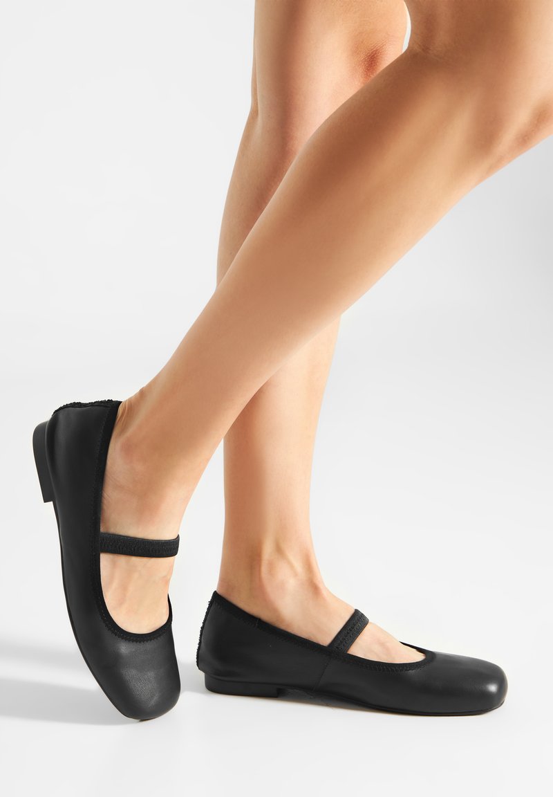 Bailarinas negras de cuero suave con punta redonda, banda elástica en el empeine y tacón bajo. Textura suave, detalles mínimos.