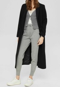 Svart lång kappa över en grå cardigan, vit topp och grå sweatpants. Vita sneakers fulländar outfiten. Strukturerade tyger är synliga.