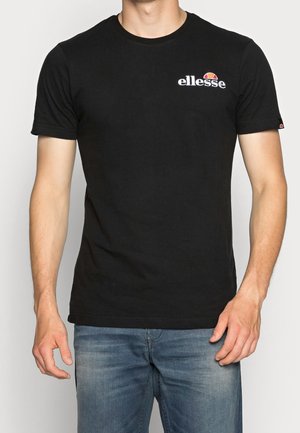 Czarna bawełniana koszulka z krótkim rękawem, okrągłym dekoltem i białym logo "ellesse" na piersi, zestawiona z jasnoniebieskimi dżinsami.