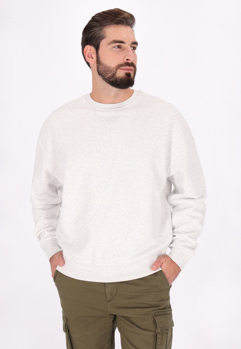 Lichtgrijze sweatshirt met ronde halslijn en ribgebreide manchetten, voorzien van een subtiele geborduurde logo. Gepaarde met olijfkleurige cargobroek.