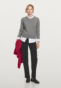 Szary sweter z dekoltem w serek na białej koszuli z kołnierzykiem, zestawiony z czarnymi spodniami ze sztruksu. Czerwony kardigan zarzucony na lewe ramię, noszony z ciemnymi mokasynami.