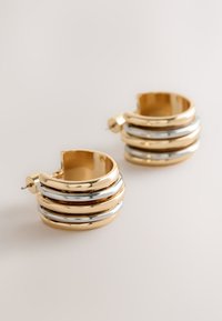 Gold and silver hoop earrings with three stacked rings, featuring a shiny finish and a small hinge for closure. Displayed on a neutral background.
