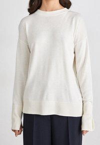 Off-white knit sweater with a ribbed crew neck and cuffs, featuring a relaxed fit and subtle textured detailing at the hem.