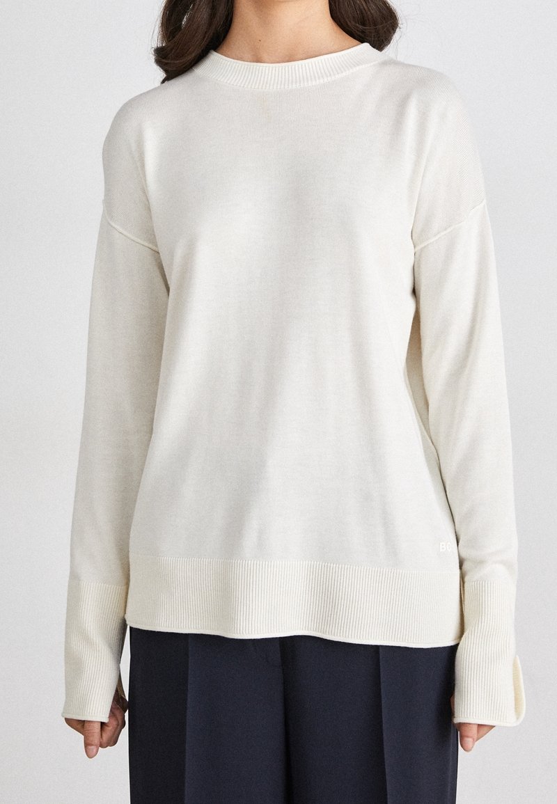 Off-white knit sweater with a ribbed crew neck and cuffs, featuring a relaxed fit and subtle textured detailing at the hem.