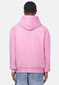Rosa Pullover-Hoodie mit einer großen Kapuze, gerippten Bündchen und einem lockeren Schnitt. Hergestellt aus weichem Baumwollstoff mit einem schlichten Design.