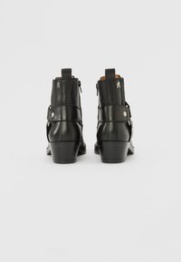 Botines de cuero negro con tacón bajo, cremallera lateral y correas decorativas. Textura suave con acentos de herrajes plateados.