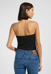 Svart ribbad off shoulder-topp i kombination med blå denimjeans som har en läder Lee-logopatch på baksidan av midjan och synliga bakfickor.