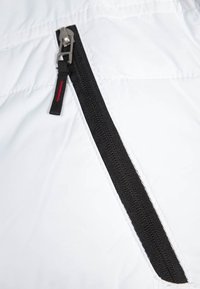 Vit tygtextur med en vertikal svart dragkedja. Dragkedjan har en silverfärgad dragtag och en röd accent på slider.