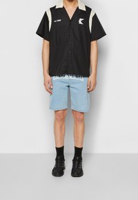Czarna koszula z krótkim rękawem z kremowymi akcentami i logo, zestawiona z jasnoniebieskimi szortami dżinsowymi z białym napisem, dopełniona czarnymi sneakerami.