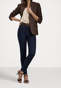 Brown textured blazer over a ruffled cream blouse, paired with dark skinny jeans and brown strappy high heels.