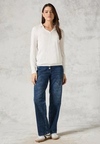 Witte blouse met lange mouwen en kraag, gecombineerd met blauwe wijde jeans. De stof lijkt zacht; de jeans hebben een knoopsluiting en een subtiele vervaging.