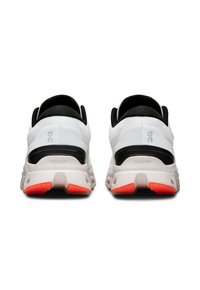 Baskets de sport blanches et noires avec une tige texturée, une semelle rembourrée et des accents orange vif au niveau des talons. Détails de logo.