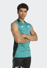 Jasnoniebieska bezrękawnik sportowy z czarnymi akcentami po bokach i logo. Czarne spodenki z jasnoniebieskimi paskami. Sportowy krój. Gładka faktura materiału.
