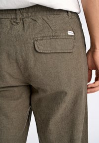 Olivgröna linnbyxor med resårmidja, med en bakficka och strukturerad tyg. Sidovy visar naturlig drapering.