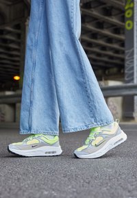 Sneakers med en grå och vit design, med neon gula accenter och meshpaneler, i kombination med vida blå denimbyxor.