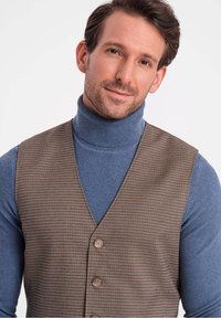 Braun karierter Weste mit drei Knöpfen über einem blauen Rollkragenpullover. Der Stoff hat eine strukturierte Oberfläche, und die Weste hat ein V-Ausschnitt-Design.