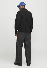 Veste décontractée noire à manches longues, associée à un pantalon en denim foncé. Une casquette bleue et des chaussures noires complètent la tenue. Design simple avec des couleurs unies.