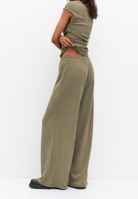 Haut tricot côtelé vert olive et pantalon à jambes larges, présentant une coupe décontractée et un tissu texturé, porté avec des chaussures à plateforme noires.