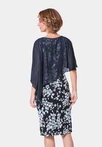 Marineblaues, florales Chiffon-Cape-Overlay über einem enganliegenden Kleid mit Schwarz-Weiß-Blumenmuster, das unterschiedliche Texturen und Muster im Stoff zur Geltung bringt.