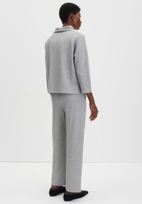Grijze trui met een opstaande kraag, oversized pasvorm en driekwart mouwen, gecombineerd met bijpassende wijde broek. Zwarte platte schoenen met studs.