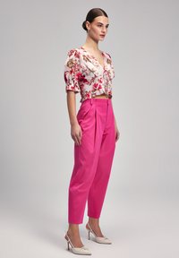 Floral cropped blouse with puff sleeves in white and pink hues paired with high-waisted, tailored bright pink trousers and white heeled shoes.
