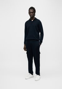 Πλεκτό πουλόβερ σε ναυτικό μπλε με γιακά, συνδυασμένο με αντίστοιχο παντελόνι cargo με τσέπες. Άσπρα αθλητικά παπούτσια ολοκληρώνουν το look, προσδίδοντας μια casual αισθητική.