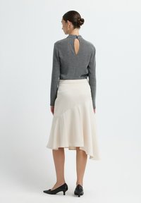 Grijze, aansluitende top met een sleutelgat aan de achterkant, gecombineerd met een crèmekleurige asymmetrische uitlopende rok. Zwarte puntige schoenen maken de outfit compleet.