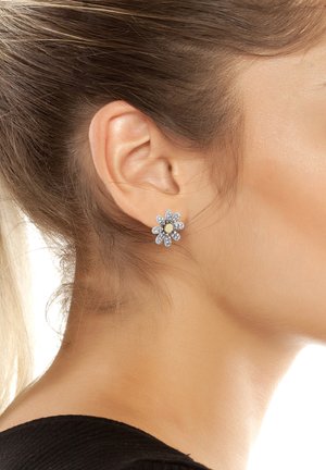 Gli orecchini a perno a forma di fiore argentati presentano pietre di rhinestone trasparenti e un accento centrale dorato. Il design è simmetrico con disposizioni simili a petali.