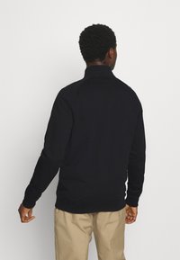 Black pullover sweater with a high collar, ribbed cuffs, and hem. Smooth texture without patterns, viewed from the back against a white background.