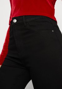 Crne traperice slim fit, s prednjim džepom, zatvaranjem na srebrni gumb i suptilnim detaljima šivanja na šavovima.