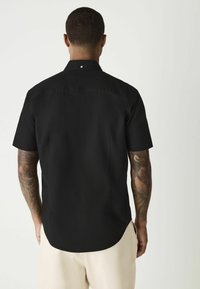 Schwarzes kurzärmliges Shirt aus glattem Stoff, mit einem spitzen Kragen, dezentem Knopfdetail und einem abgerundeten Saum.