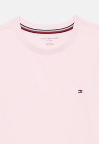 Light pink t-shirt with a round neckline, featuring a small embroidered logo. Ribbed collar includes red, white, and navy stripes.