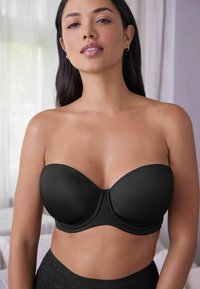 Svart strapless-bh med slätt, matt tyg, formade kupor och byglar, med en central sömdetalj och sömlösa kanter.