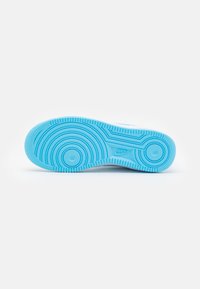 Kék talpú Nike edzőcipő, amelyen kör alakú mintázatok láthatók, a középen a Nike logójával, fehér háttér előtt.