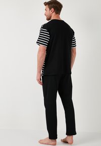 Tricou negru din bumbac cu mâneci în dungi, asortat cu pantaloni de pijama negri. Croială lejeră, cu decolteu rotund și un design simplu.