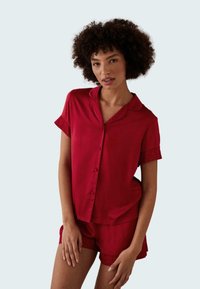 Red satin pajama set featuring a short-sleeve button-up top and matching shorts with lace trim on sleeves and hem. Smooth texture.