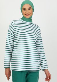 Maglietta bianca a maniche lunghe con righe verticali verdi, accompagnata da un hijab verde abbinato. Il tessuto appare morbido con una vestibilità comoda.