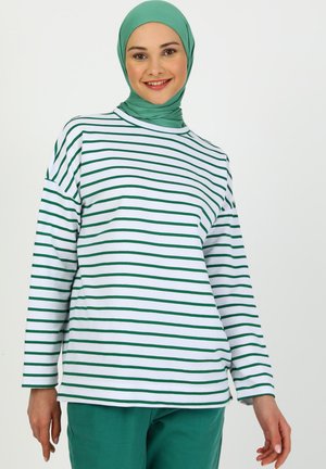Langärmliges weißes Oberteil mit grünen vertikalen Streifen, begleitet von einem passenden grünen Hijab. Der Stoff wirkt weich und hat eine lässige Passform.