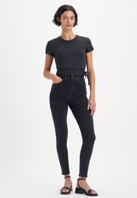 Svart tettsittende topp med korte ermer og knyte-detalj i midjen, kombinert med høytlivs svarte skinny jeans og svarte sandaler med stropper.