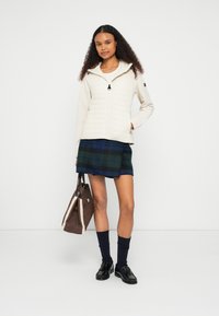 Ανοιχτό μπεζ μπουφάν με φερμουάρ και κουκούλα, με υφή στο μπροστινό μέρος, συνδυασμένο με μπλε καρό φούστα. Μαύρα παπούτσια και κάλτσες, καφέ τσάντα με λεπτομέρειες από shearling.