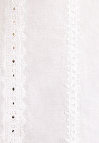 Tissu blanc avec deux bordures de dentelle verticales, présentant des bords festonnés à gauche et une bande délicatement décorée à droite.