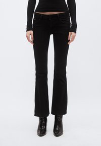 Vaqueros negros acampanados con cintura de talle medio, bolsillos delanteros y trabillas para cinturón. La tela tiene una textura suave y un ligero estiramiento, que mejora el ajuste.