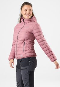 Lyserød pufjakke med en tætsiddende design, høj krave, forklaringslynlås og sidelommer; parret med mørke tekniske bukser med lynlåse.