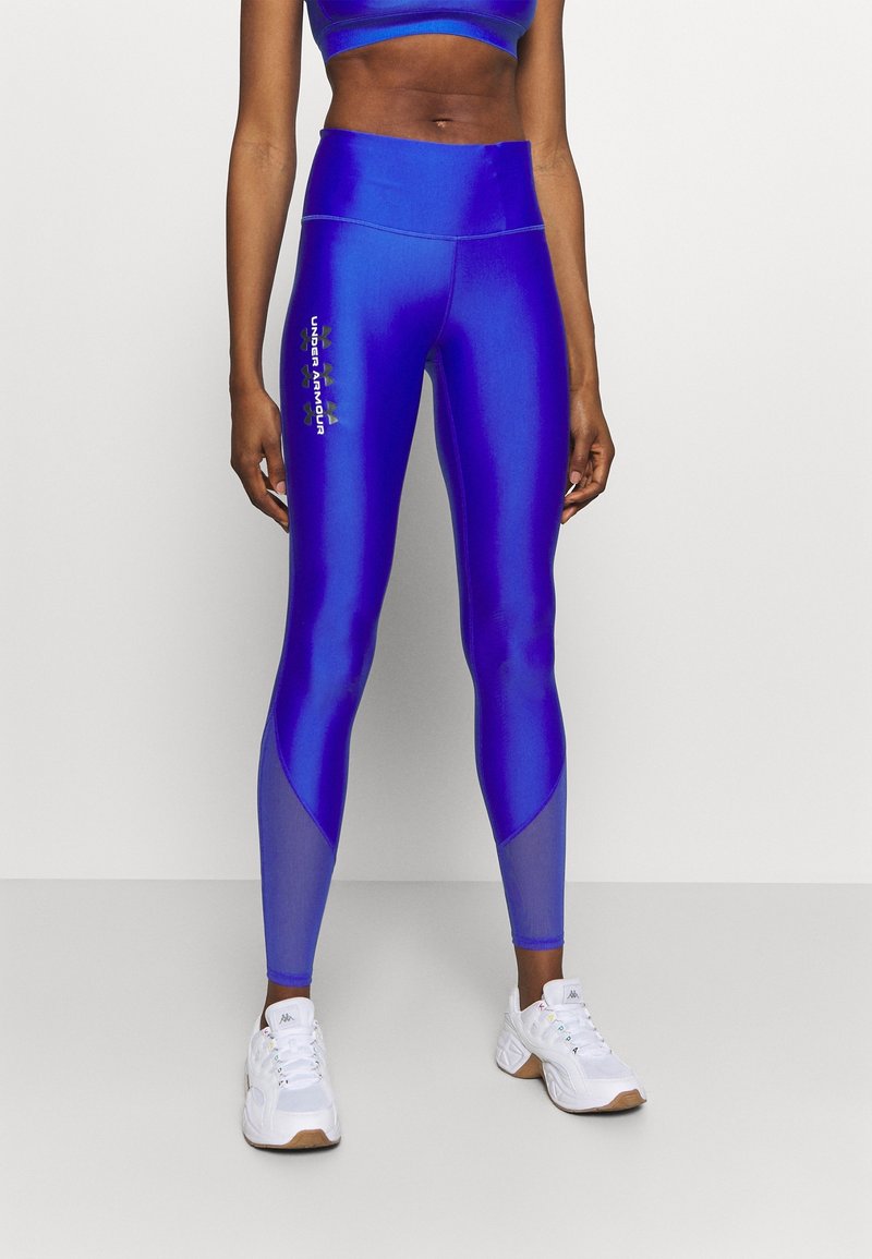 Korkeavyötäröiset siniset legginsit, joissa on kiiltävä pinta. Niissä on tummansiniset kontrastipaneelit ja vihreä "Under Armour" -logo sivussa.