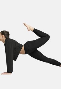 Svart träningsoutfit som består av en åtsittande långärmad topp och högmidjade leggings. Modellen utför en yogapose på alla fyra med ett ben utsträckt.