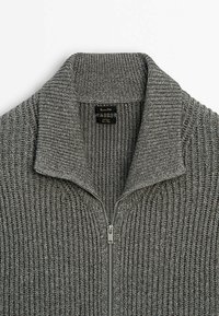 Maglione grigio a maglia con colletto zip, texture a coste e dettagli di cucitura in evidenza. La zip presenta un tirante metallico.