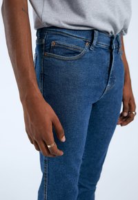 Jeans in denim blu con vestibilità slim, caratterizzati da un classico design a cinque tasche, cuciture arancioni e una superficie liscia.