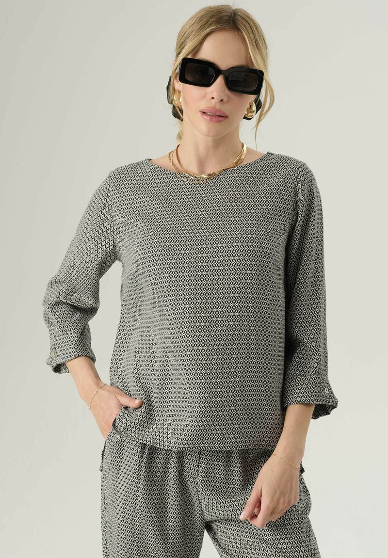 Top a righe bianche e nere con maniche a tre quarti, scollatura tonda e vestibilità rilassata, abbinato a pantaloni coordinati. Tessuto testurizzato.