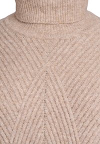 Beige neuleoppa turtleneck, jossa on ribbipinta ja pehmeä, pörröinen rakenne.