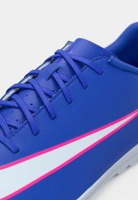 Kék sportcipő sima szintetikus felsőrésszel, fehér és rózsaszín díszítéssel az oldalon, és összekötve azonos színű kék fűzőkkel.